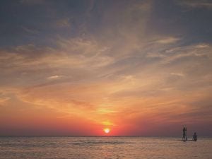 Sunset over the ocean with two people standing on a paddleboard.