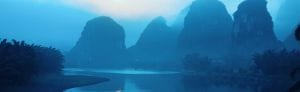 Scenic view of limestone karst formations over a river in a misty landscape.