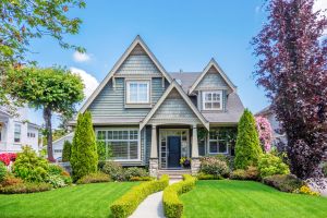 Beautiful gray house with a well-maintained front yard and colorful trees in a suburban neighborhood.